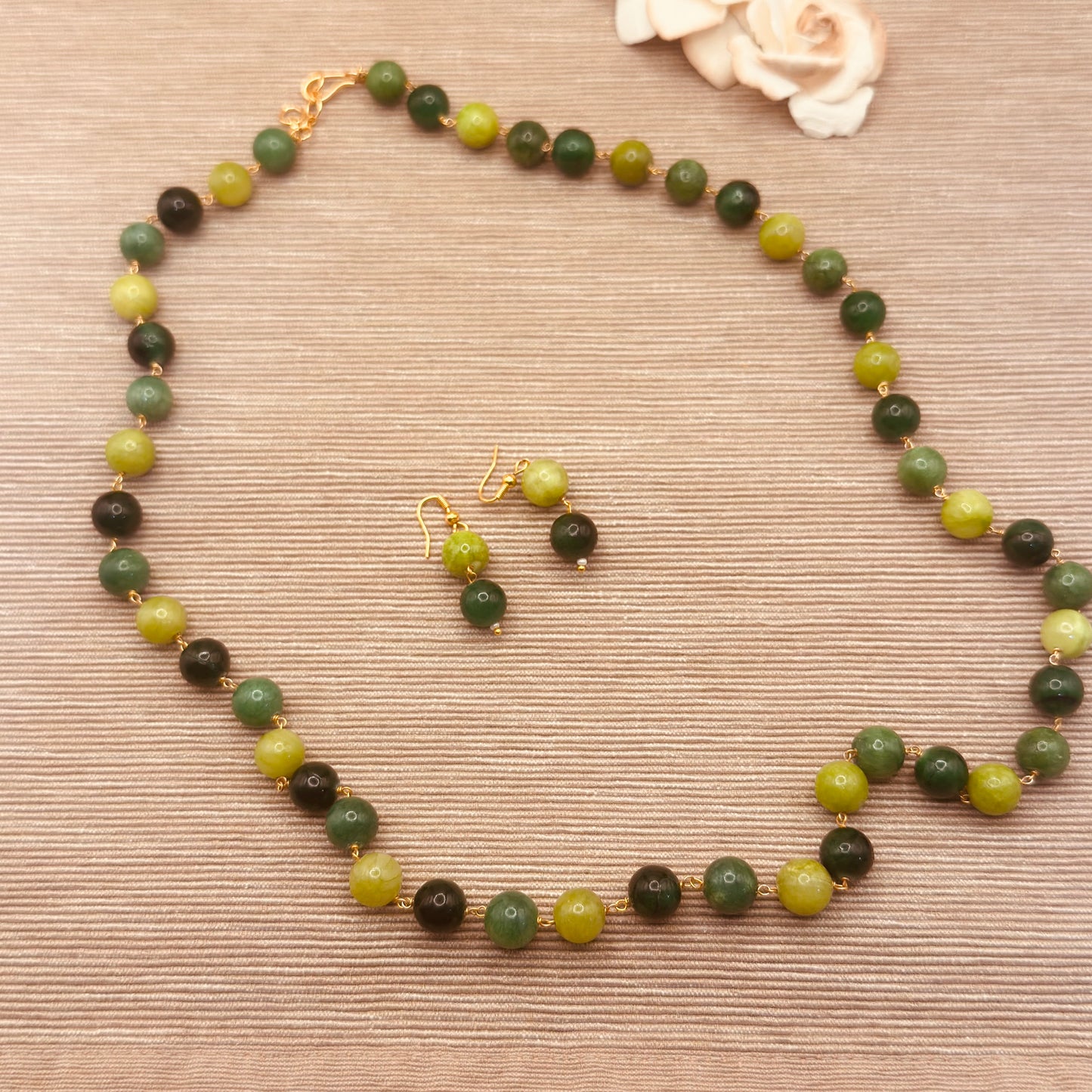A beaded necklace and matching drop earrings.
This set features a necklace of 10mm semi precious dyed quartz round beads in shades of olive green, dark forest green, and light yellow-green, separated by small gold spacers, with gold-tone hooks and clasps.