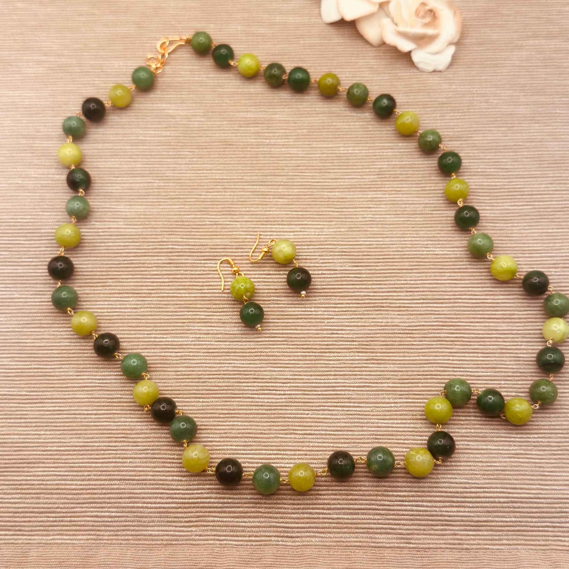 A beaded necklace and matching drop earrings. 
This set features a necklace of  10mm semi precious dyed quartz round beads in shades of olive green, dark forest green, and light yellow-green, separated by small gold spacers, with gold-tone hooks and clasps.